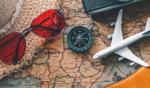 Travel essentials including a straw hat, red sunglasses, plane tickets, and a toy airplane on a vintage world map.