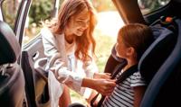 Mother buckling her young child into a car seat with a warm smile on her face.