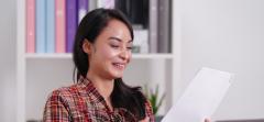 Smiling woman reading a document in an office setting with colorful binders in the background.