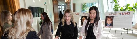 Attendees networking at the Gryphons on Bay Street event, with Lang School of Business and notable alumni signage in the background.