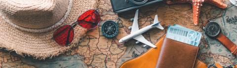 Travel essentials including a straw hat, red sunglasses, plane tickets, and a toy airplane on a vintage world map.