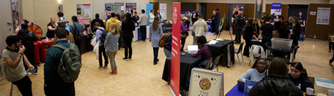 Students interacting with booths at a career fair, exploring opportunities at a university networking event with various tables and informational displays.