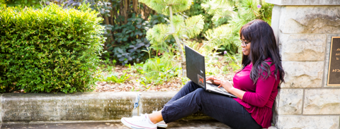 Female U of G student using laptop while sitting beside a fountain