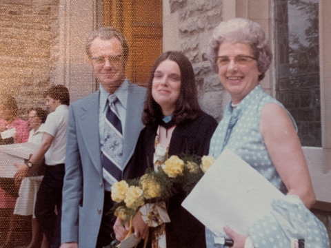A sepia tinted photo of Valerie at her convocation holding flowers between her two smiling parents