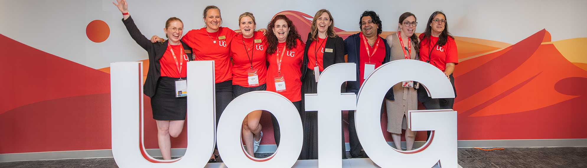 Group of University of Guelph alumni and staff posing together at an event in front of a U of G sign.