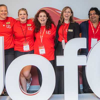 Group of University of Guelph alumni and staff posing together at an event in front of a U of G sign.