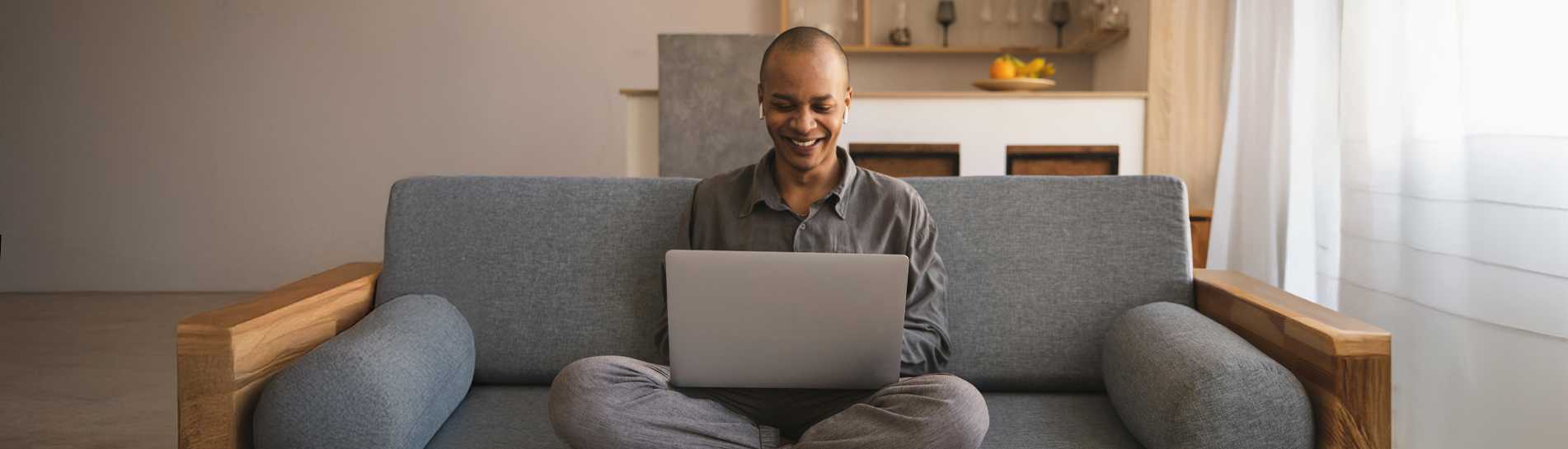 Person sitting on a sofa at home, smiling while using a laptop to participate in an online webinar. 