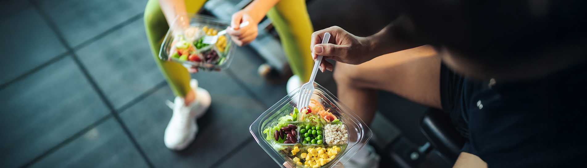 Two individuals in athletic attire eating salads