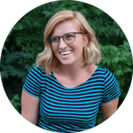 A professional portrait of Dr. Kristina Kupferschmidt, B.Eng '14, PhD '25, a woman with shoulder-length blonde hair, wearing glasses and a blue and black striped top, smiling outdoors with green foliage in the background.