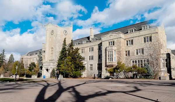 Daytime view of Johnston Hall at the University of Guelph, a historic building surrounded by trees, with clear skies in the background.