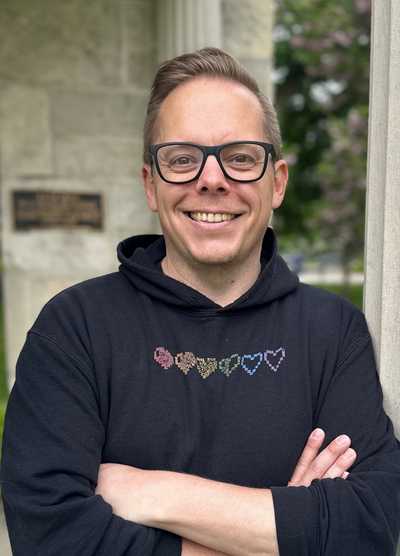 Portrait of Alumni Volunteer Award 2024 recipient Daniel J. Gillis, BSc ’00, MSc ’02, PhD ’10, smiling with crossed arms while standing in front of a stone column.