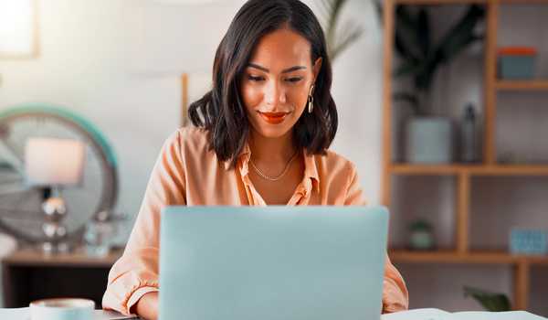 Confident woman working on a laptop in a modern home office setting, smiling and focused on her task.