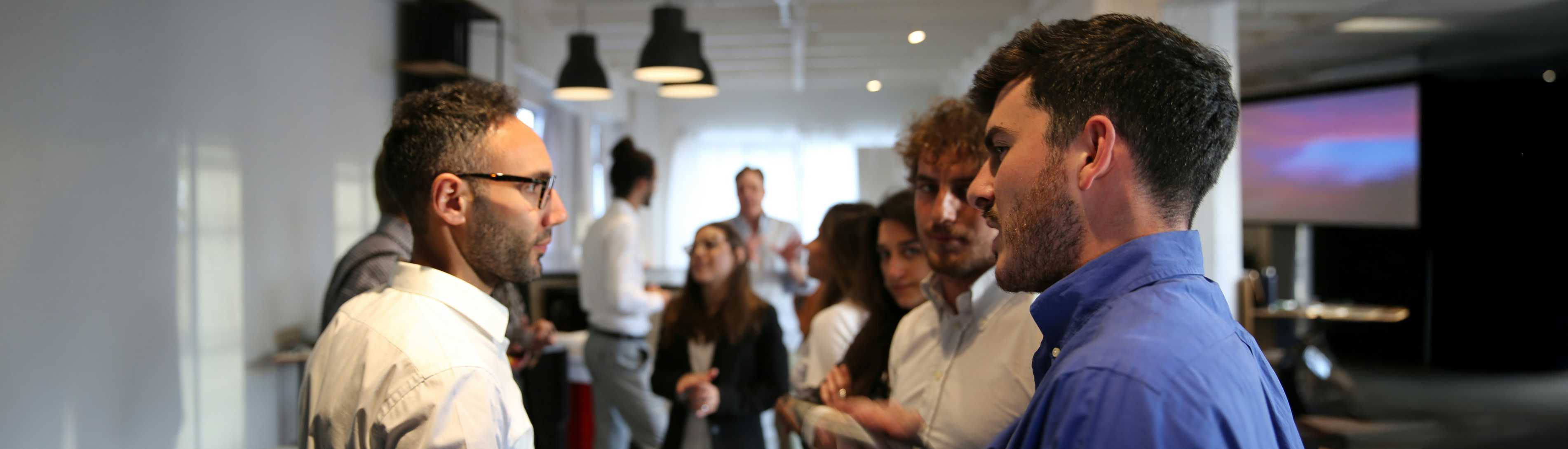 Group of University of Guelph OAC alumni socializing at a modern indoor event space, with some individuals holding drinks and others engaged in conversation. 