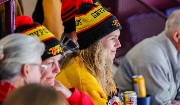 A group of University of Guelph fans wearing Gryphons-themed winter hats and sweaters enjoying a sporting event, with drinks on the table in front of them.